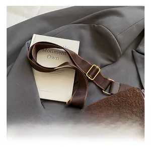 Detail view of adjustable shoulder strap and golden metal buckle on brown plush saddle bag