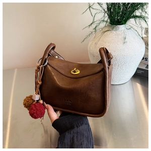 Close-up of brown retro shoulder bag featuring a gold metal twist lock and plush charm detail