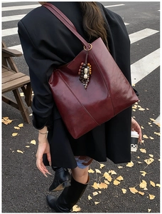 Detail view of burgundy leather tote bag featuring vintage wooden bead charm and stitching