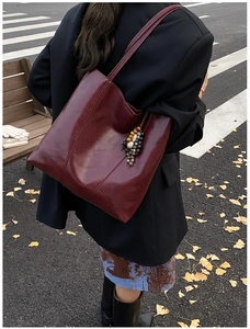 Chic burgundy leather tote bag with a unique beaded grape charm against autumn leaves