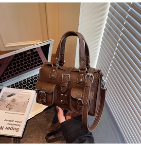 Detail of a brown lychee pattern leather handbag with vintage metal buckles and rivets