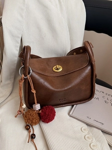 Brown leather retro crossbody bag with metal lock and decorative charm on white fabric