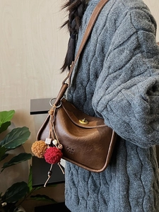 Vintage brown leather pillow bag with decorative plush charms and side logo embossing