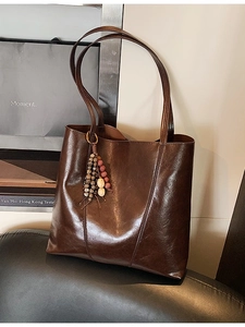 Deep brown oil wax leather tote bag with vintage bead charm on a leather chair