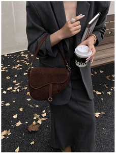 Model wearing a dark brown teddy fleece saddle bag with leather straps on autumn gravel