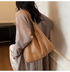 Detailansicht einer braunen geflochtenen Leder-Tote-Bag an einem Modell mit einem Trendmantel