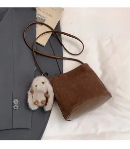 Dettaglio della borsa a secchiello marrone opaco con ciondolo a coniglio in peluche su blazer