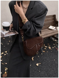 Brown faux shearling saddle bag with metal D charm shown in a cozy outdoor autumn setting