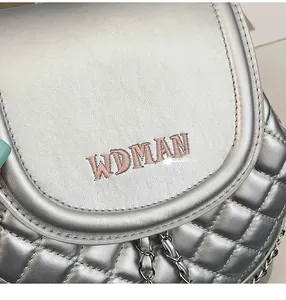 Close-up of silver quilted backpack with metal chain strap and WDMAN pink embroidery