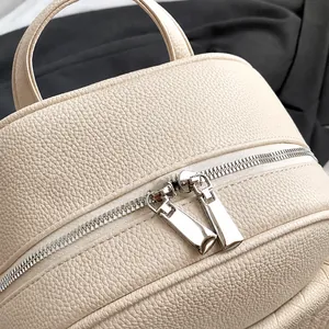 Detail showing smooth double silver zippers on cream-colored lychee textured leather bag