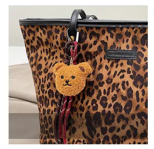 Nahaufnahme eines braunen Teddybär-Anhängers mit gewebtem Band an einer Leoparden-Tragetasche