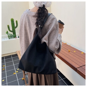 Back view of a large black canvas tote bag worn by a model in a minimalist outdoor setting