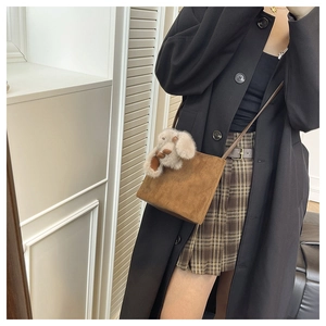 Borsa a secchiello in camoscio marrone con ciondolo peluche e trench nero elegante