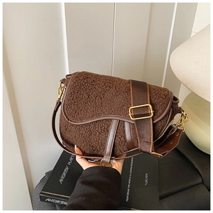 Detail of dark brown saddle bag featuring fuzzy shearling texture and wide fabric strap