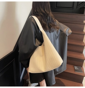 Detail der beigen geflochtenen Hobo-Tasche mit geometrischer Textur auf einer Lederjacke