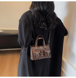 Detail of dark brown lychee textured handbag featuring retro double front buckle pockets
