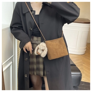 Borsa a secchiello minimalista marrone opaca con ciondolo a coniglio su cappotto lungo