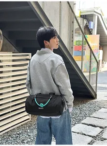 Detail einer schwarzen Reisetasche mit blaugrünem Knotengriff getragen von einem Modell