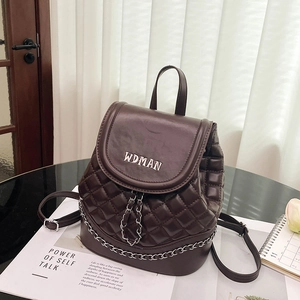 Detail view of dark brown quilted backpack with silver chain and brand logo on a magazine
