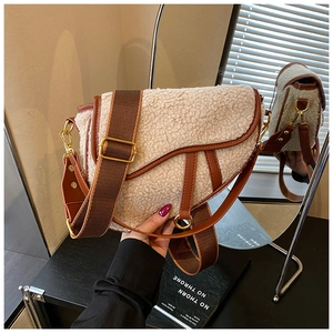 Detail of white shearling saddle bag with brown leather trim and wide fabric strap