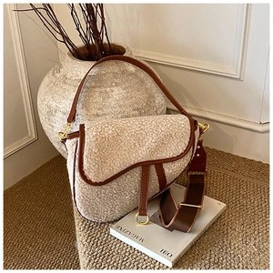 Detailed view of cream faux shearling saddle bag with brown leather trim and golden D-ring