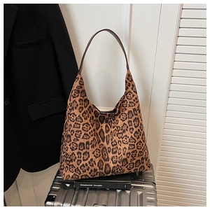 Close-up of leopard print Hobo bag with slim brown handles next to a silver suitcase