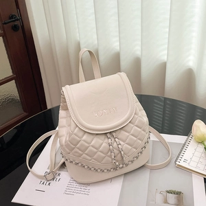 Close-up of beige quilted mini backpack with WOMAN embossed text and silver chain detail