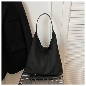 Detail view of a large black suede tote bag placed on a silver metallic suitcase