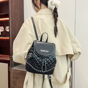 Detail of a black quilted mini backpack with silver chain strap worn on a beige coat