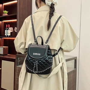 Detail of black quilted mini backpack featuring metal chain and white logo on flap