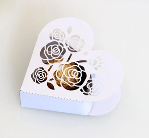 Detail of white heart gift box featuring intricate laser-cut rose design and chocolate
