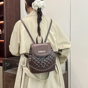Detail view of brown quilted PU leather backpack with chain accent on beige trench coat