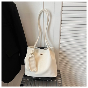 Dettaglio della borsa tote bianco crema testurizzata con pochette su una valigia