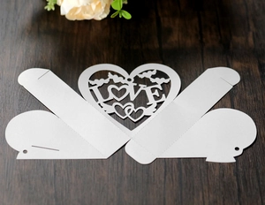 Flat lay of laser-cut white paper wedding favor box featuring an intricate heart and LOVE motif