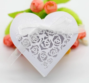 Close-up of white heart-shaped favor box with laser-cut rose patterns and silk ribbon