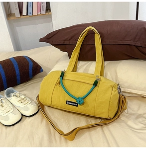 Detail der gelben Nylon-Zylindertasche mit grünem Knotengriff auf beigem Bettzeug