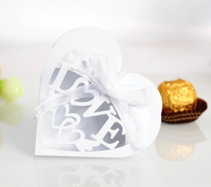 Close-up of white laser-cut LOVE heart candy box with silk bow and hollow pattern