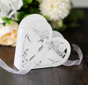 Detailed laser-cut heart candy box with bird patterns and white ribbon on dark wood