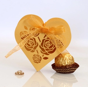 Detail showing golden heart-shaped laser cut favor box with rose design and ribbon