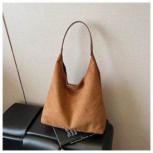 Detailed view of brown suede hobo bag with dark leather strap on a minimalist bench