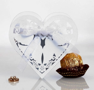 Detail of laser-cut heart-shaped wedding favor box with white ribbon and floral patterns