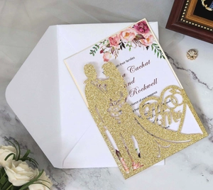 Close-up of laser-cut gold glitter wedding invitation with Mr & Mrs silhouette and flowers
