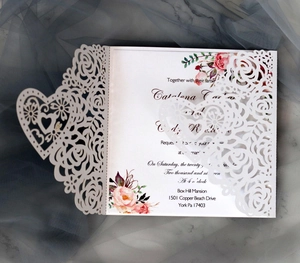 Detail of laser-cut rose and heart patterns on elegant white wedding invitation card