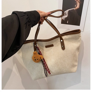 Beigefarbene Cord-Tasche mit braunen Ledergriffen und kleinem Teddybär-Anhänger im Detail