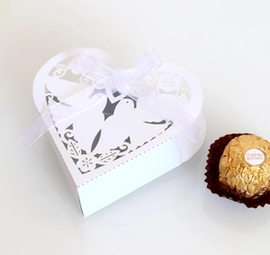 Macro shot of white heart-shaped laser-cut wedding favor box with organza ribbon