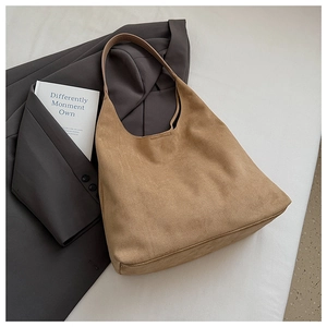 Detail of a brown suede half-moon tote bag with slender leather straps on a grey blazer