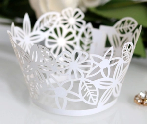 Macro shot of white laser-cut cupcake wrappers with intricate floral and leaf patterns
