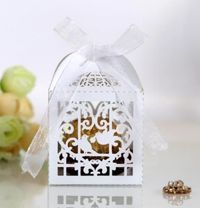 Detail of laser-cut birdcage wedding favor box with white ribbon and gold chocolate