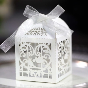 Close-up of laser-cut white favor box with bird cage pattern and silver organza ribbon