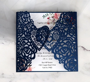 Detailed laser-cut heart and rose patterns on a navy blue wedding invitation cover